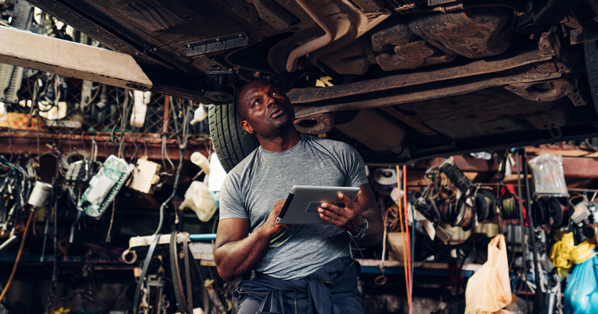 Powerful Auto Repair Software Scheduling: Use It or Lose It 4 auto technician working underneath a car using Auto Repair Software Scheduling on his tablet